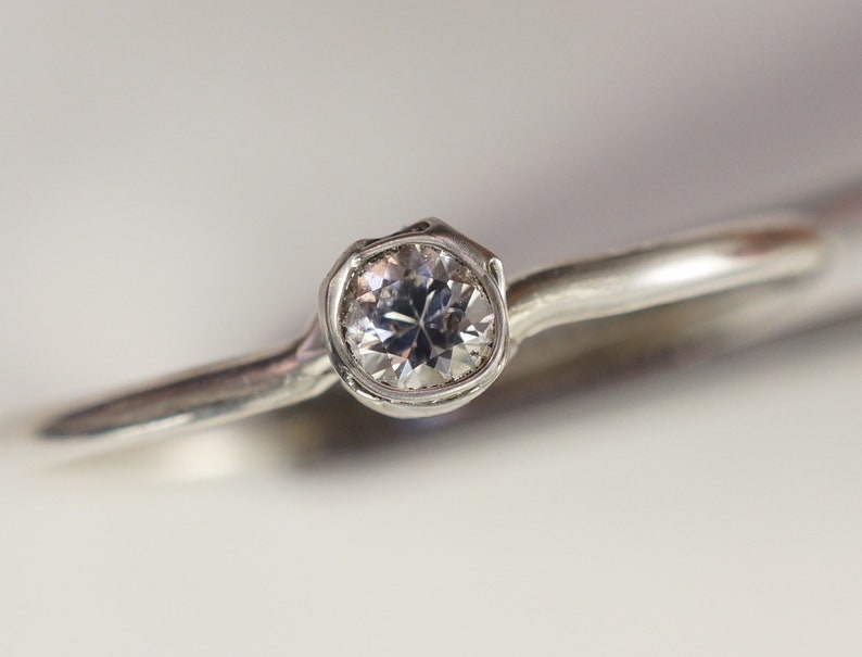 May include: A silver ring with a single round diamond set in a bezel setting.
