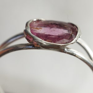 K&ouml;nnte beinhalten: Ein silberner Ring mit einem rosafarbenen Edelstein, der in einer einzigartigen, unregelm&auml;&szlig;igen Form gefasst ist.