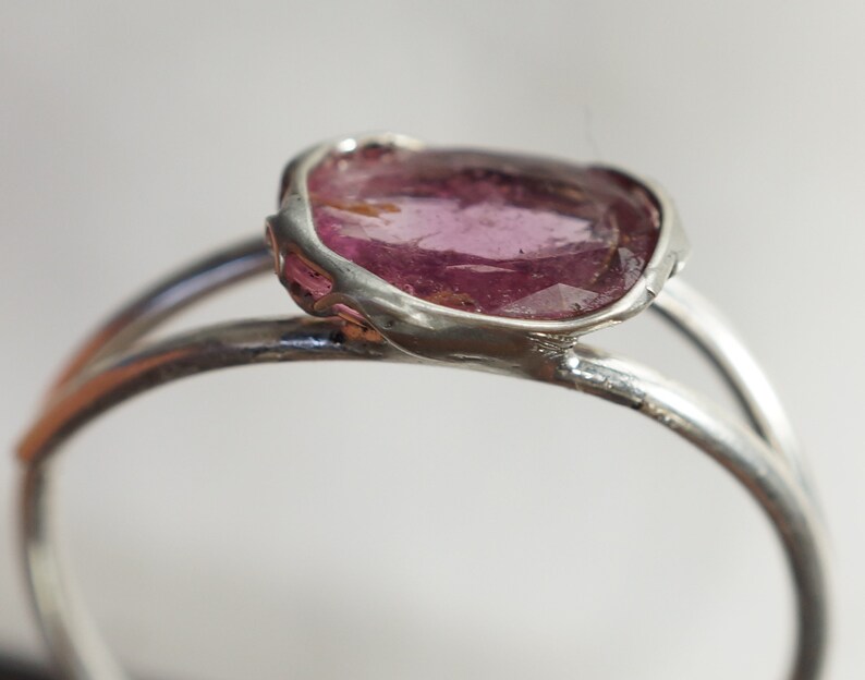 K&ouml;nnte beinhalten: Ein silberner Ring mit einem rosafarbenen Edelstein, der in einer einzigartigen, unregelm&auml;&szlig;igen Form gefasst ist.
