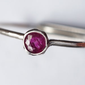 May include: A simple silver band ring with a small, round, faceted ruby gemstone.