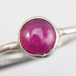 May include: A silver ring with a pink gemstone set in a bezel setting.