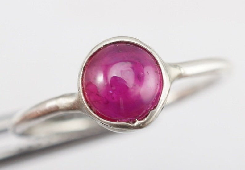 May include: A silver ring with a pink gemstone set in a bezel setting.