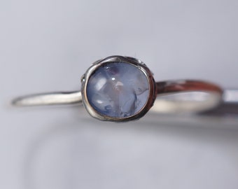 Puede incluir: Un anillo de plata con una piedra preciosa azul claro engastada en un engaste de plata. El anillo tiene una banda texturizada.