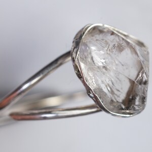 May include: A silver ring with a large, clear, faceted crystal set in the center. The crystal is rough and has a natural, unpolished look.