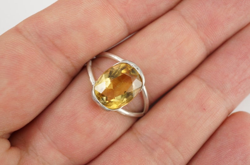 May include: A silver ring with a large, oval-shaped, yellow gemstone.