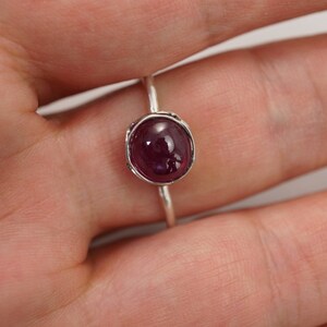 May include: A silver ring with a deep red oval gemstone set in a textured bezel.