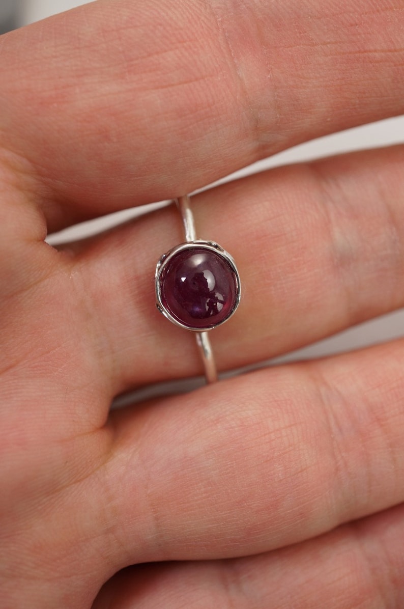 May include: A silver ring with a deep red oval gemstone set in a textured bezel.