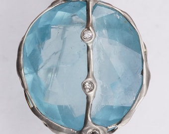 Può includere: Un pendente in argento con una grande pietra preziosa azzurra con una superficie sfaccettata. La gemma è impreziosita da quattro piccoli diamanti e una montatura in argento. Il pendente è tenuto da una chiusura in argento.