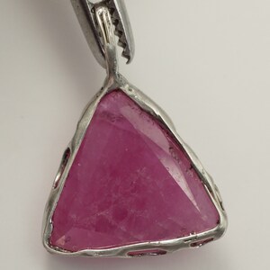 May include: A silver pendant featuring a triangular pink gemstone set in a silver frame.