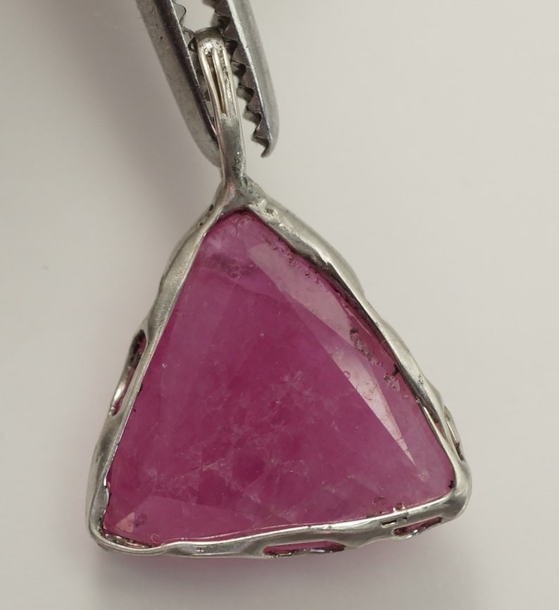 May include: A silver pendant featuring a triangular pink gemstone set in a silver frame.