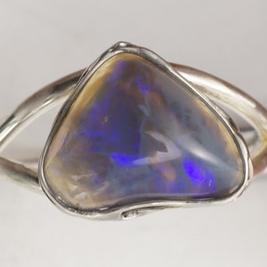 Puede incluir: Un anillo de plata con una gran piedra de &oacute;palo iridiscente. El &oacute;palo tiene un color azul, morado y blanco.