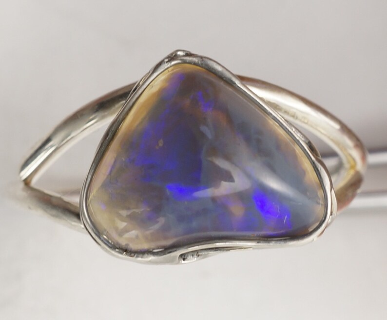 Puede incluir: Un anillo de plata con una gran piedra de &oacute;palo iridiscente. El &oacute;palo tiene un color azul, morado y blanco.