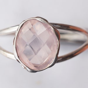 Puede incluir: Un anillo de plata con una piedra ovalada de color rosa claro. La piedra tiene un corte facetado y est&aacute; engastada en una banda de plata.