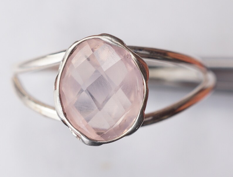 Puede incluir: Un anillo de plata con una piedra ovalada de color rosa claro. La piedra tiene un corte facetado y est&aacute; engastada en una banda de plata.