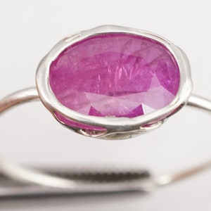 Op de afbeelding: Een zilveren ring met een grote ovale roze edelsteen gezet in een delicate zilveren zetting.