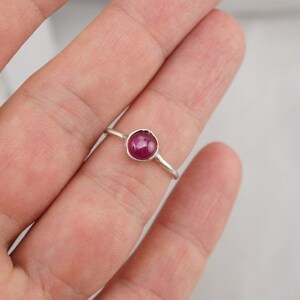 May include: A silver ring with a round, dark pink gemstone.