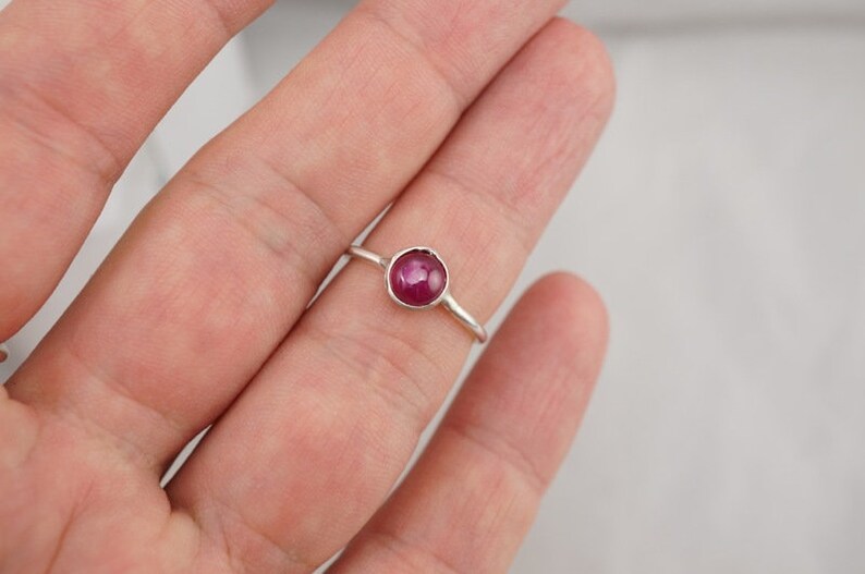 May include: A silver ring with a round, dark pink gemstone.