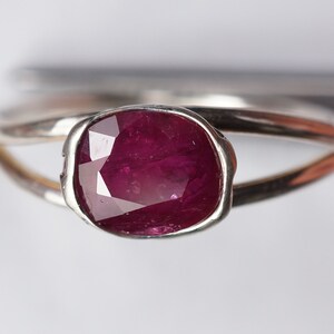 Op de afbeelding: Een zilveren ring met een dieprode robijn-edelsteen gezet in een bezel-setting. De ring heeft een eenvoudig, elegant ontwerp.