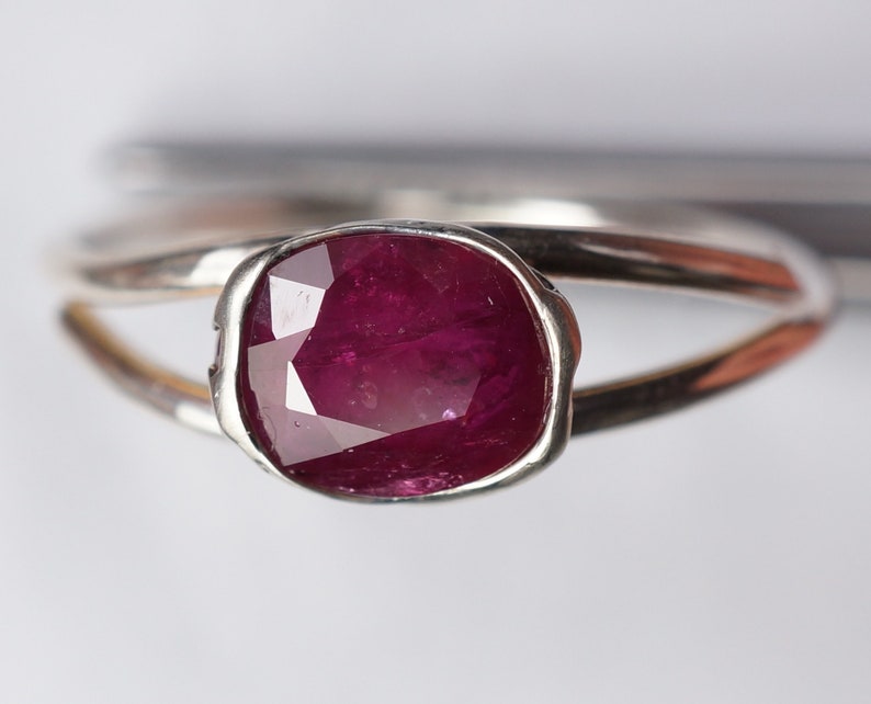 Op de afbeelding: Een zilveren ring met een dieprode robijn-edelsteen gezet in een bezel-setting. De ring heeft een eenvoudig, elegant ontwerp.