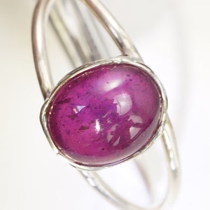 Puede incluir: Un anillo de plata con una gema grande, ovalada, de color magenta intenso. La gema est&aacute; engastada en un bisel y la banda del anillo tiene un dise&ntilde;o simple y elegante. El anillo se muestra sobre un fondo blanco.