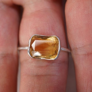 May include: A silver ring with a large, rectangular, yellow gemstone set in a bezel setting.
