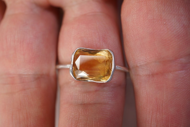 May include: A silver ring with a large, rectangular, yellow gemstone set in a bezel setting.