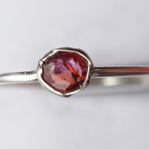 Op de afbeelding: Een zilveren ring met een roze en rode edelsteen in een bezel setting.