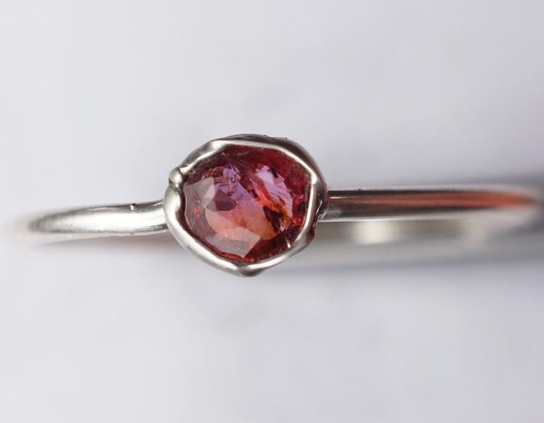 Op de afbeelding: Een zilveren ring met een roze en rode edelsteen in een bezel setting.