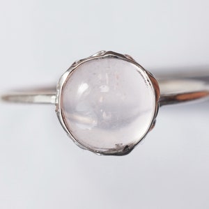 Puede incluir: Un anillo de plata con una piedra redonda, clara y rosa p&aacute;lida engastada en un engaste texturizado.