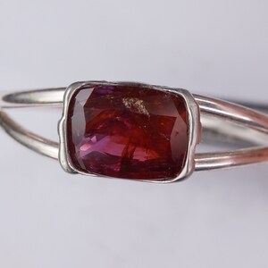 Pu&ograve; includere: Un anello d'argento con una pietra preziosa sfaccettata di colore rosso scuro incastonata in una montatura a castone.