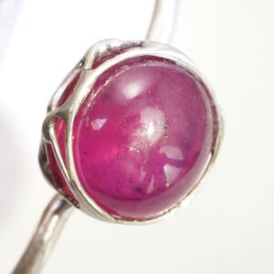 May include: A silver ring with a large, round, cabochon-cut ruby gemstone set in a delicate, wire-wrapped setting.