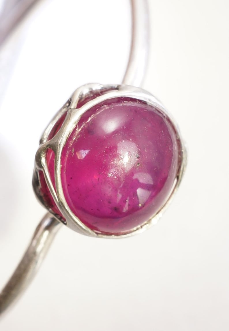 May include: A silver ring with a large, round, cabochon-cut ruby gemstone set in a delicate, wire-wrapped setting.