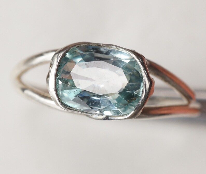 May include: A silver ring with a light blue oval gemstone set in a bezel setting.