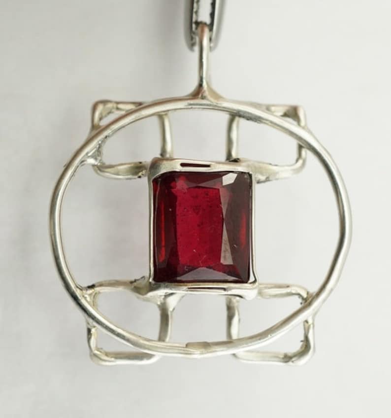 May include: A silver pendant with a geometric design featuring a red gemstone in the centre.