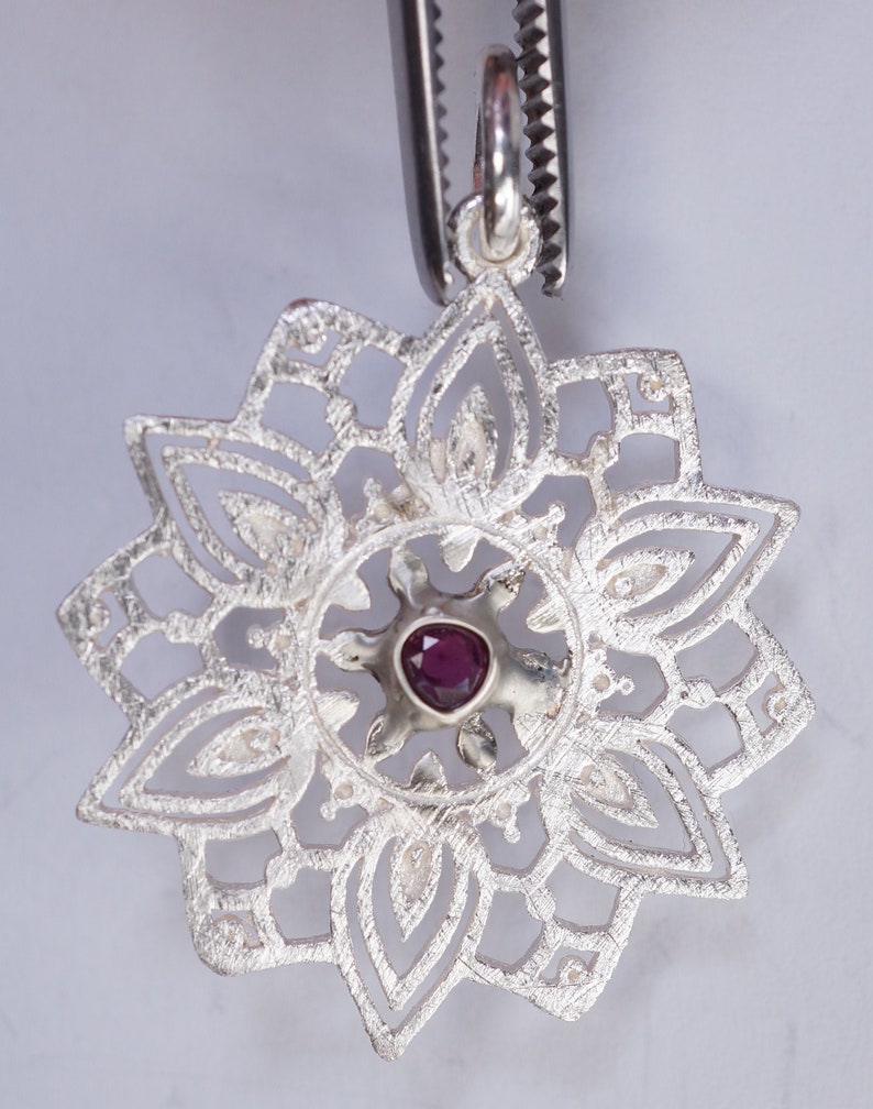 May include: Silver pendant with a delicate, intricate design featuring a central purple gemstone. The pendant is shaped like a flower with multiple layers of petals.