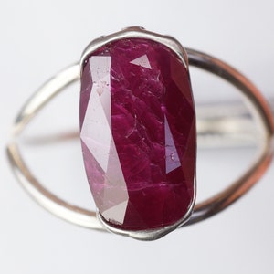 Op de afbeelding: Een zilveren ring met een grote, gefacetteerde robijn. De robijn is diep rood van kleur en heeft een licht onregelmatige vorm.