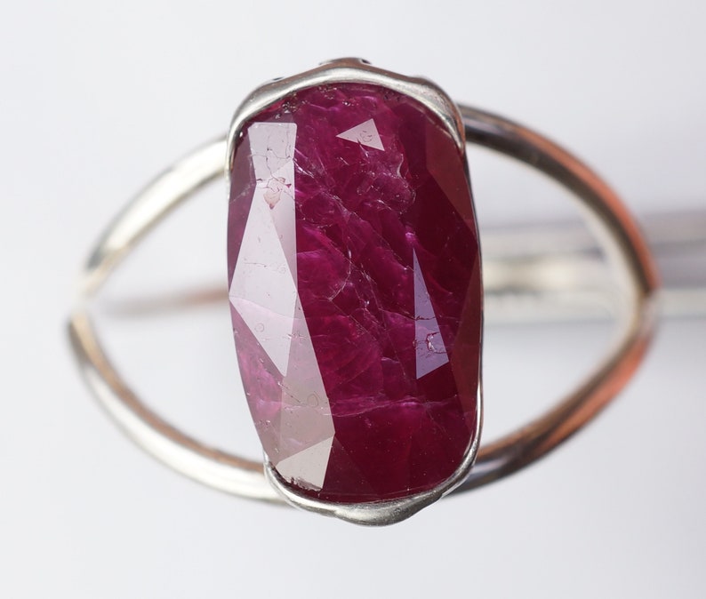 Op de afbeelding: Een zilveren ring met een grote, gefacetteerde robijn. De robijn is diep rood van kleur en heeft een licht onregelmatige vorm.