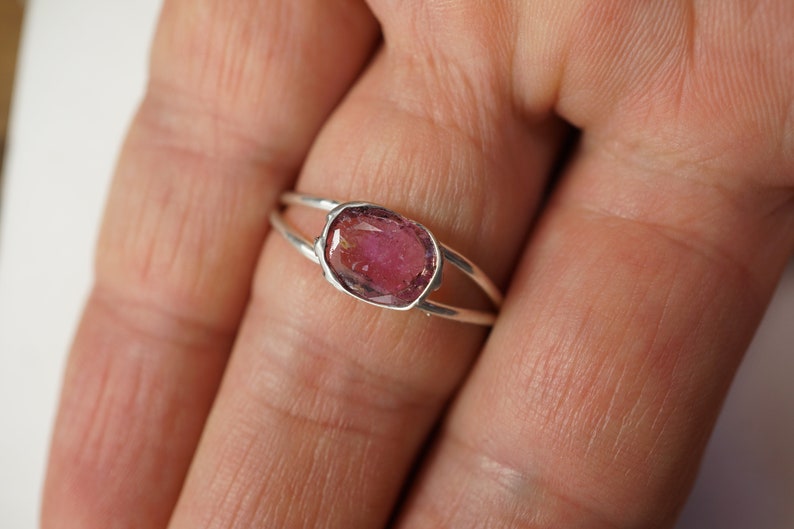 K&ouml;nnte beinhalten: Ein silberner Ring mit einem rosafarbenen Edelstein, der in einer Zargenfassung gefasst ist. Der Ring hat ein Doppelband-Design.