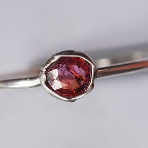 Op de afbeelding: Een zilveren ring met een roze edelsteen in een getextureerde zetting.