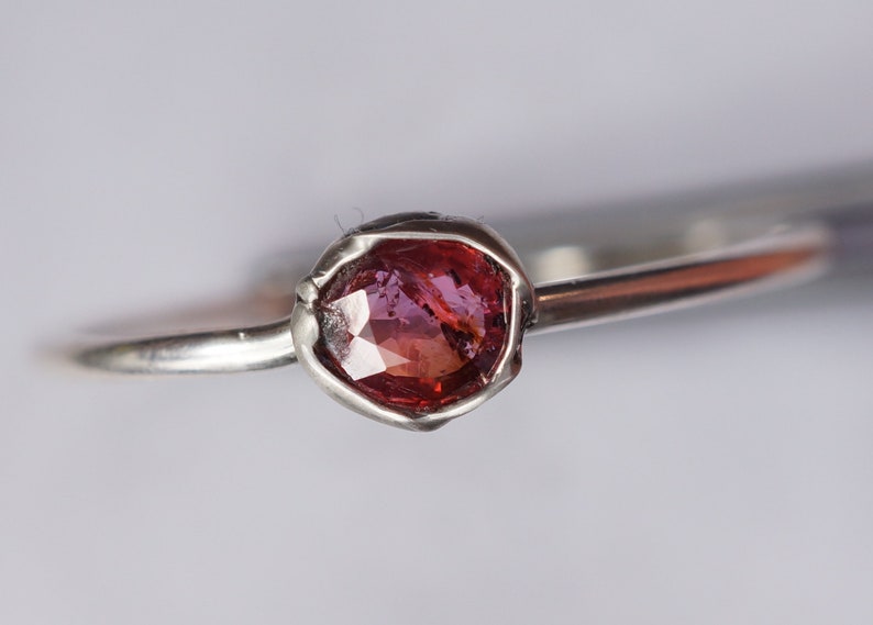 Op de afbeelding: Een zilveren ring met een roze edelsteen in een getextureerde zetting.