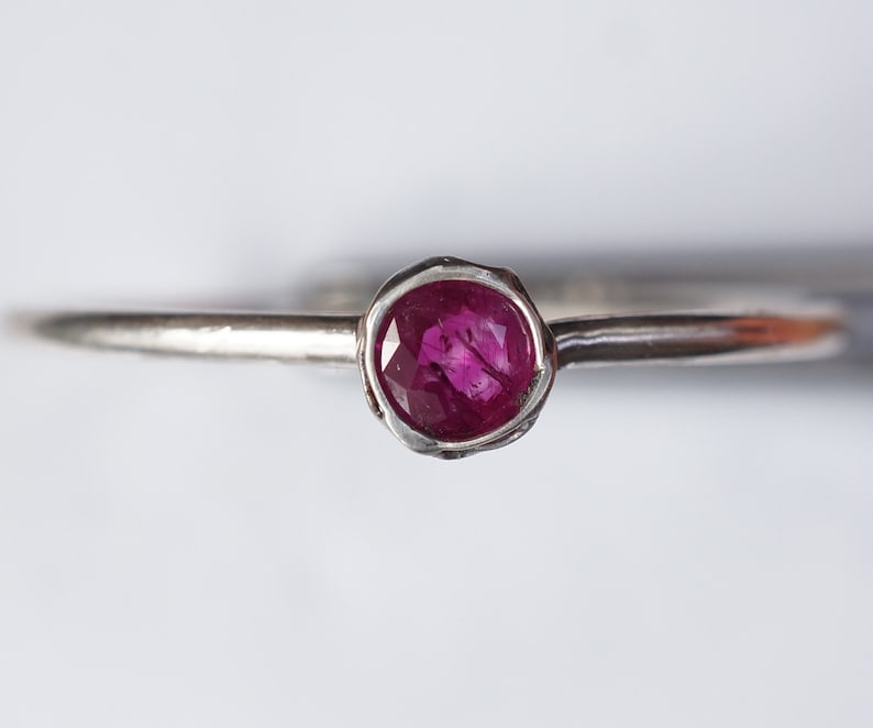 May include: A silver ring with a deep pink ruby gemstone set in a textured band.