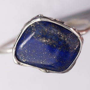 Puede incluir: Un anillo de plata con una gran piedra de lapisl&aacute;zuli azul oscuro de forma irregular engastada en el centro. La piedra tiene un aspecto moteado y brillante.