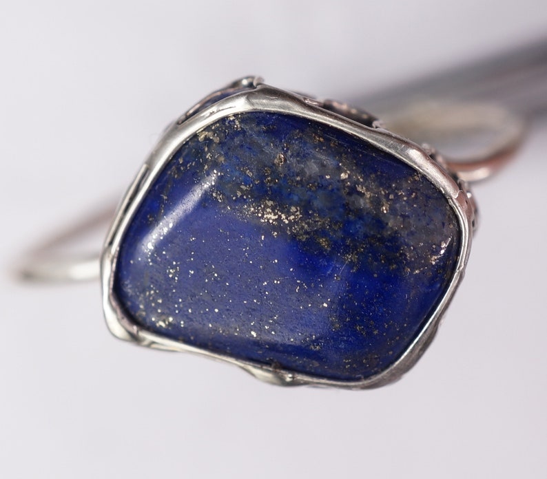 Puede incluir: Un anillo de plata con una gran piedra de lapisl&aacute;zuli azul oscuro de forma irregular engastada en el centro. La piedra tiene un aspecto moteado y brillante.
