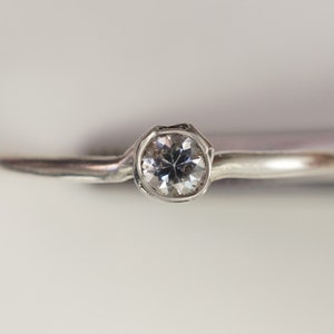 May include: A silver ring with a single round clear gemstone.