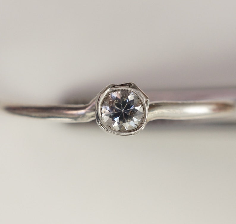 May include: A silver ring with a single round clear gemstone.