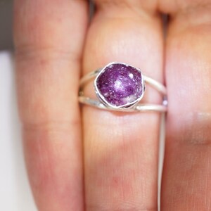 May include: A silver ring with a pink and purple gemstone set in a bezel setting. The ring has a delicate, open design.