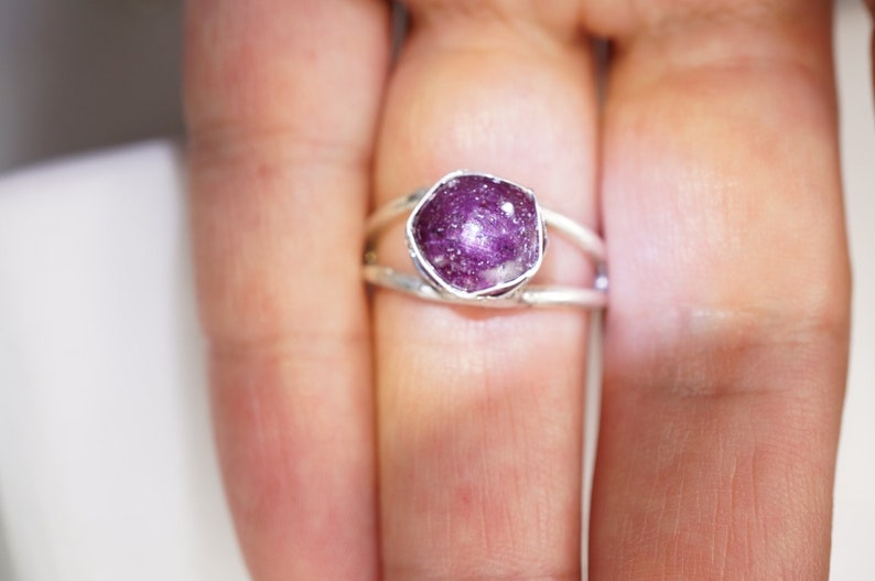 May include: A silver ring with a pink and purple gemstone set in a bezel setting. The ring has a delicate, open design.