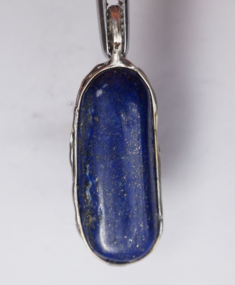 May include: A silver pendant with a large, oval-shaped lapis lazuli stone. The stone is a deep blue color with gold flecks throughout.