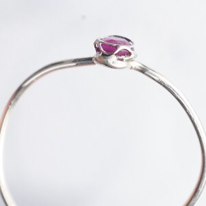 K&ouml;nnte beinhalten: Ein zarter Silberring mit einem kleinen, rosafarbenen Rubin, der in einer filigranen, durchbrochenen Fassung gefasst ist.