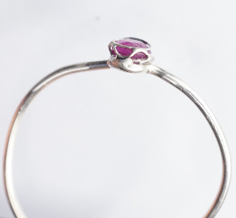 K&ouml;nnte beinhalten: Ein zarter Silberring mit einem kleinen, rosafarbenen Rubin, der in einer filigranen, durchbrochenen Fassung gefasst ist.